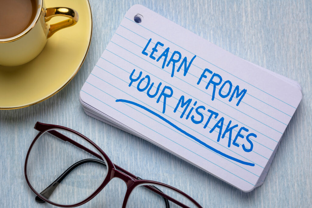 Postcard on a desk saying "Learn from your mistakes" next to glasses and a cup of tea
